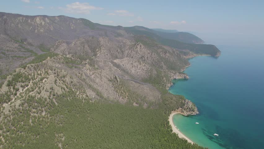 An aerial view of picturesque mountains, Lake Baikal bays with turquoise water, and yachts carrying tourists. A summer lakeside getaway.