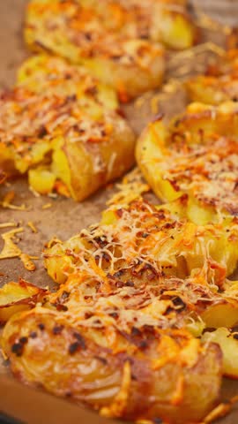 Vertical 4K 25fps slow motion close up video of unrecognizable chef hand adding chopped green onions on unbaked smashed potatoes with shredded cheese. Dark table background with copy space.