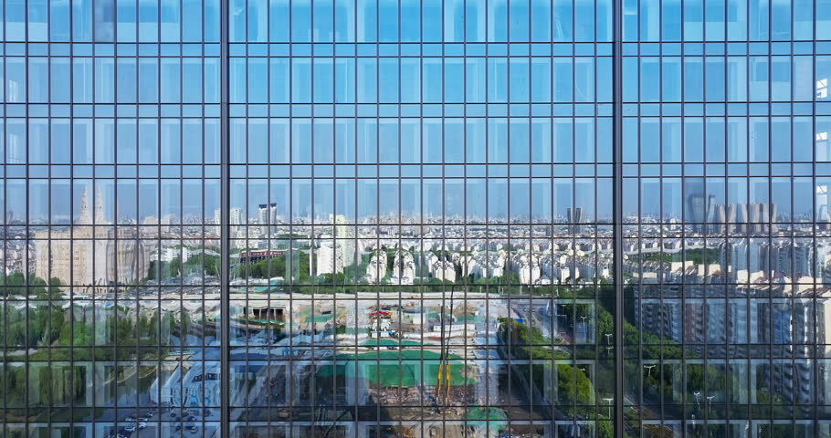 Reflection of Suzhou city skyline and active construction site on a modern glass skyscraper facade during daytime, China.