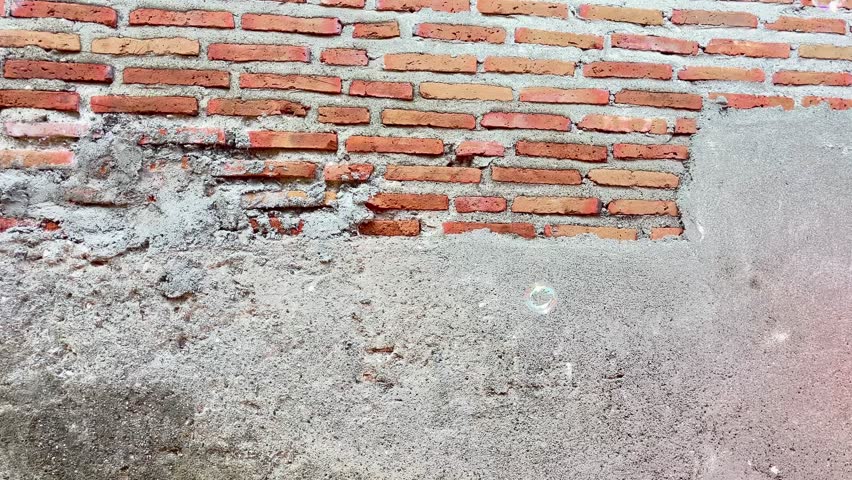A cluster of iridescent soap bubbles float against a blurred brick wall