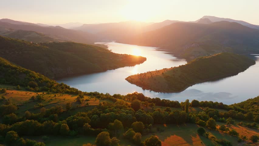 Kardzhali reservoir Arda river horseshoe bend panoramic drone view sunset golden hour orange sun light green mountain hills summer travel destination Bulgaria Rhodope landscape.