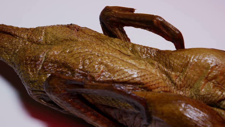 Slow pan over the crispy brown skin of a whole roasted duck showing the wings and legs on a white platter under studio lighting