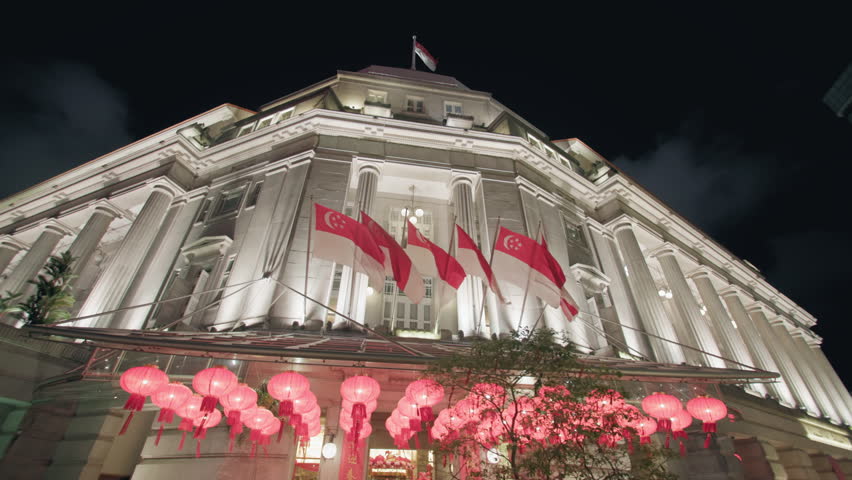 Night view of the illuminated Fullerton building with Singapore flags highlighting historic architecture and vibrant urban streets in the heart of Asia