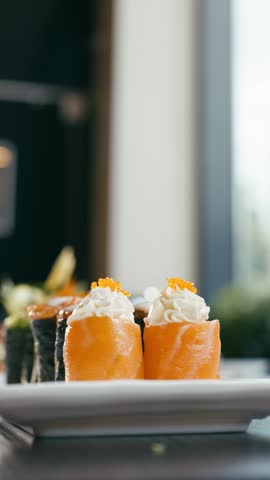 Close up of chopsticks picking up a delicious philadelphia sushi roll with salmon, cream cheese, and tobiko from a plate in a restaurant. Vertical
