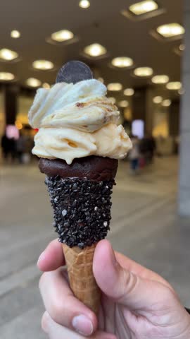 Male hand holding a chocolate and vanilla ice cream cone with dark sprinkles in a japanese mall