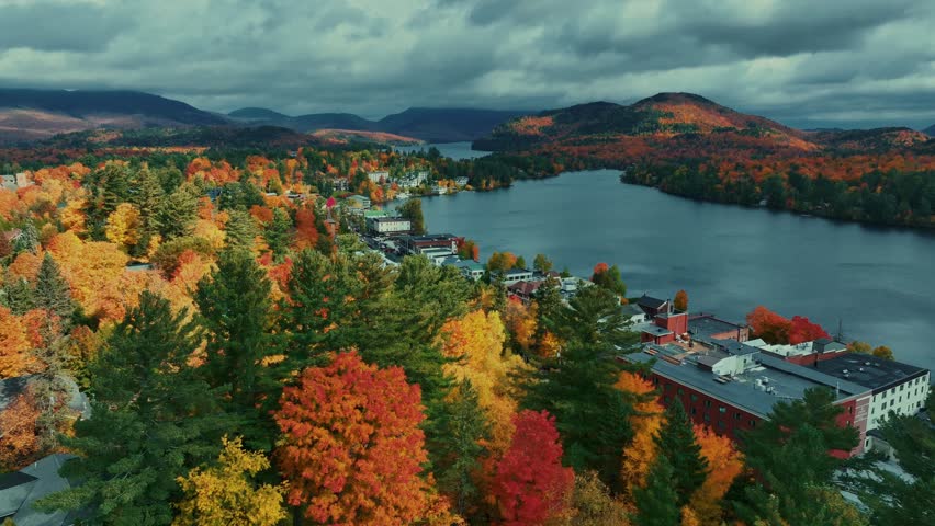 Adirondack Mountain, New York State. Aerial view of a town nestled beside a lake during autumn, with mountains in the background.