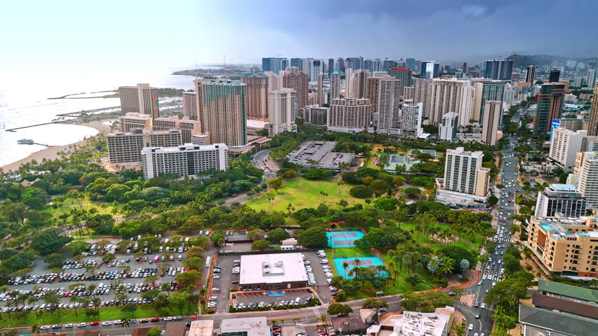 Picturesque green park with a large parking lot in the middle. Aerial perspective on the cityscape of luxurious Waikiki, Hawaii, USA.