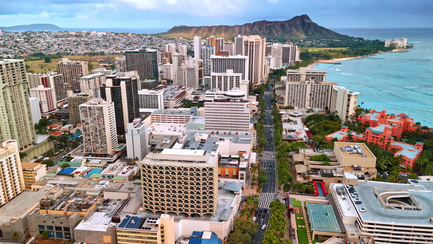 Flight over the road along the shore of Waikiki, Honolulu, Hawaii, USA. Aerial perspective on the Diamond Head Crater at backdrop.