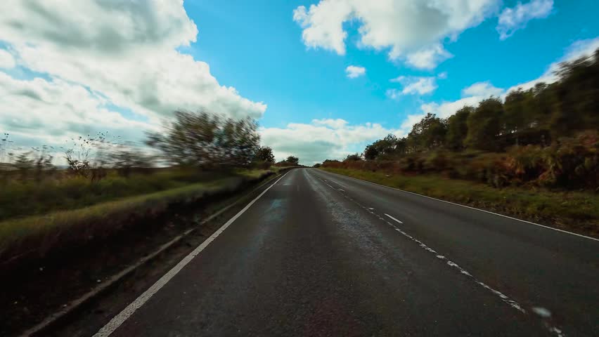 Car driving along open countryside highway under bright sky and moving toward distant horizon POV. Vehicle traveling on straight rural road surrounded by green fields symbolizing exploration and