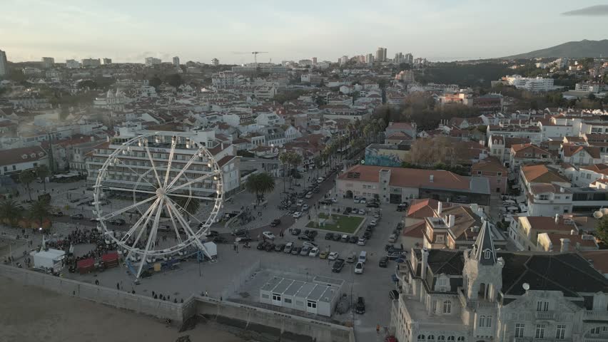 An aerial view of the Ferris wheel by the harbor in Cascais, Portugal, overlooking the Atlantic coast and vibrant town during golden hour