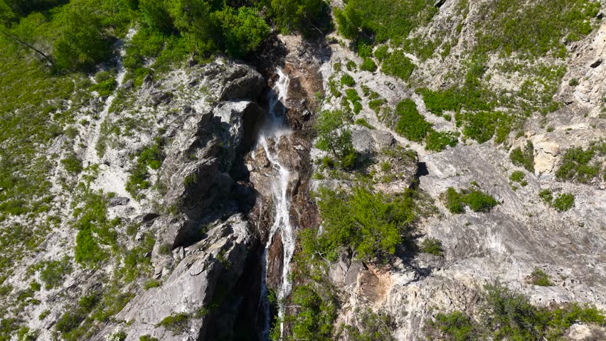 Vertical drone aerial shot flying downwards over the Shirlak waterfall, then tilting up to reveal a majestic panorama of high Altai mountains.