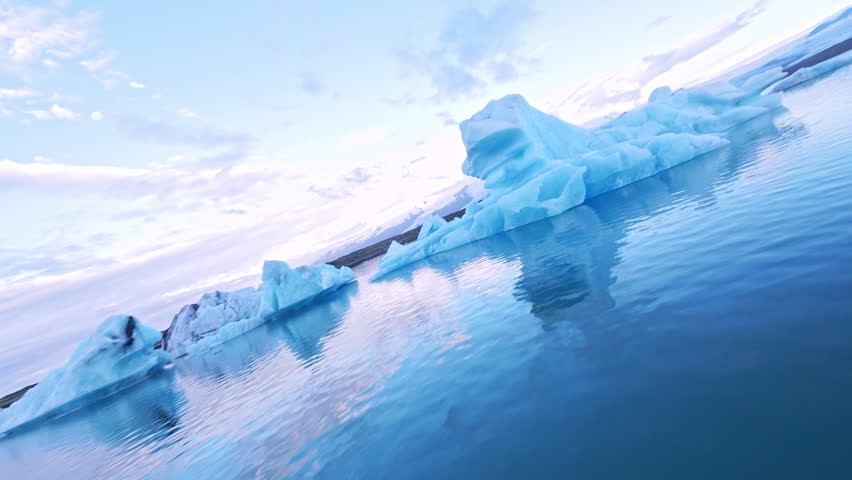 Dynamic FPV drone flight skimming above and between deep glacier crevasses on glacier, Iceland. Cinematic aerial footage revealing blue ice formations and dramatic glacial landscape.