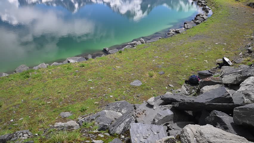 Tranquil mountain lake with mirrorlike reflections, green shoreline, and snowcapped Swiss Alps under summer clouds near Mürren.