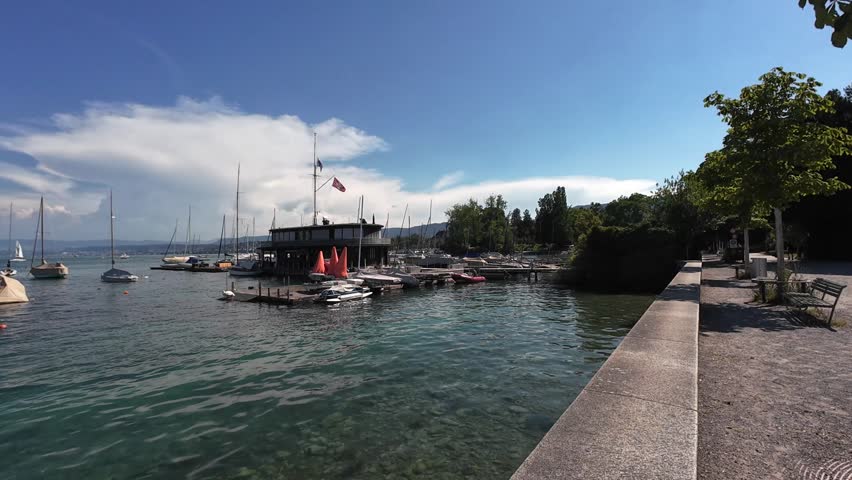 Peaceful view of Lake Zurich with clear water, boats and the surrounding urban landscape under sunny summer weather. Ideal footage of a popular European waterfront destination.