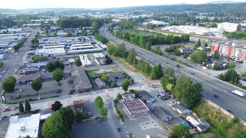 Warehouse distribution hub interstate 167 runs parallel to storage facilities defining Kent landscape. Geometric rooftops deep green trees fill frame under clear skies, forming arteries in WA. USA