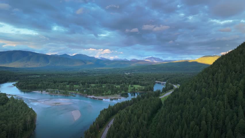 The winding Flathead River cuts gracefully through dense evergreen forests beneath a dramatic evening sky in scenic northwestern Montana, USA. July 1, 2024. 
