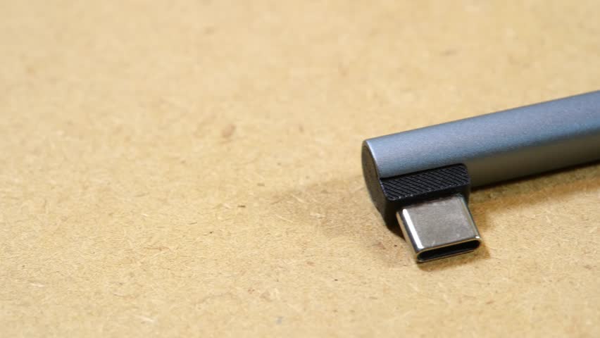 Small gray right-angle USB-C DAC audio adapter with exposed male connector on beige background, pocket digital-to-analog converter dongle for smartphones and devices without a headphone jack