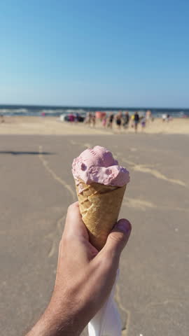 Hand Holding Pink Ice Cream Cone on Sunny Beach with Soft Focus Seaside Background