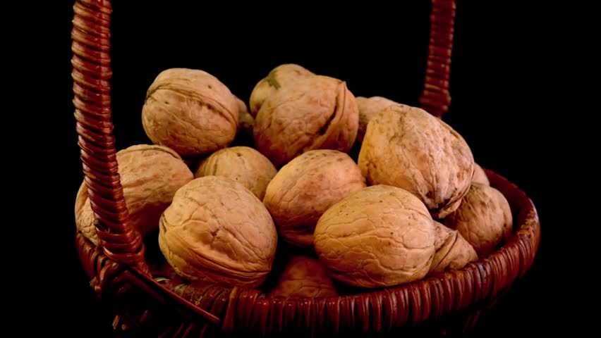 A close-up shot of raw, unpeeled whole walnuts piled inside a brown rustic wicker basket, slowly rotating against a solid black background. Perfect for healthy diet, organic food, and autumn harvest themes.
