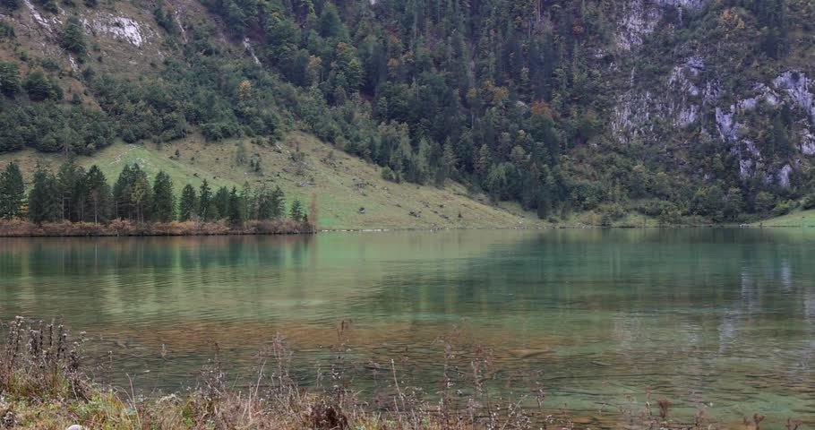 Mountain landscape with a crystal clear green lake reflecting the surrounding pine forest and slopes