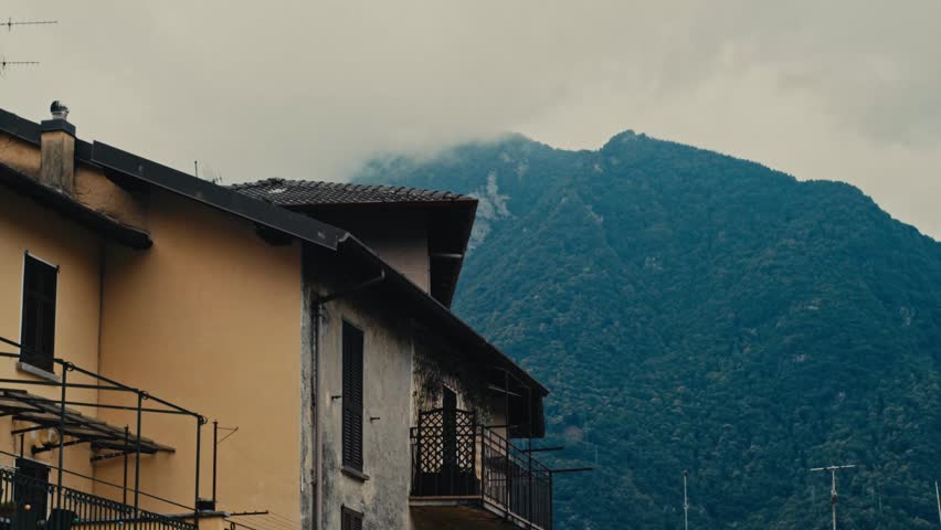 A traditional Italian house sits before a dramatic cloudy Alpine mountain.