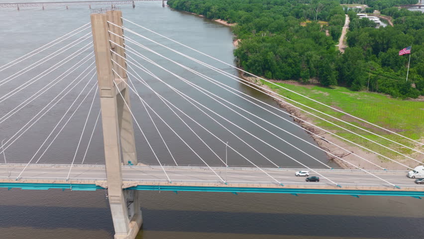 Semi across a cable-stayed Mississippi River span, midday in Quincy IL. Border between Illinois and Iowa. Ideal establishing shot for supply-chain, river-commerce, and infrastructure documentaries.