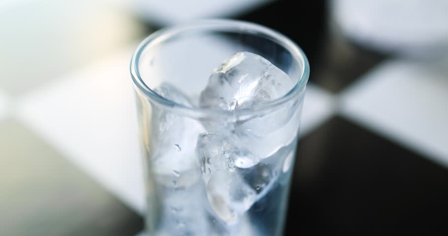 Clear water pouring from a glass bottle into an ice-filled glass. Close-up shot, freshness, purity, hydration, healthy lifestyle, and refreshing beverage