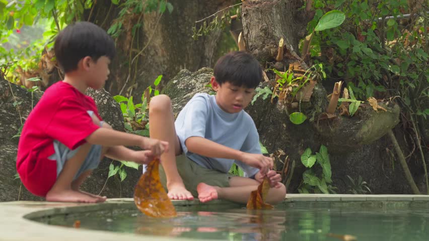 Two young boys play with leaves by the pool sides