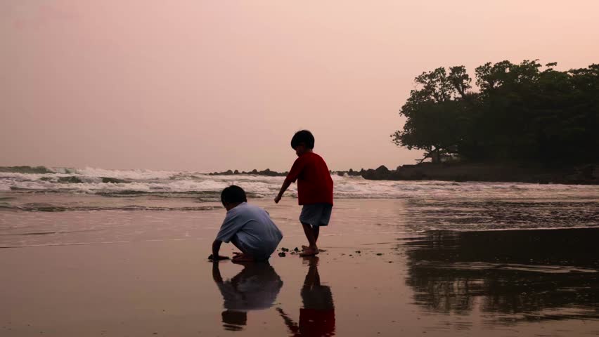 Two children dig in the sand at the beach, building sand castle together