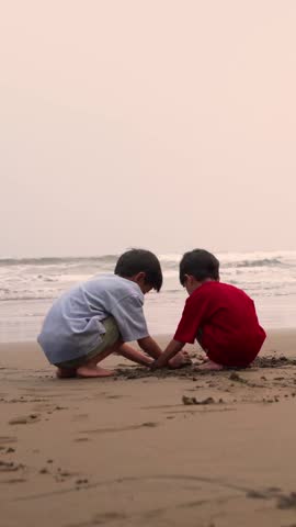 Two children dig in the sand at the beach, building sand castle together