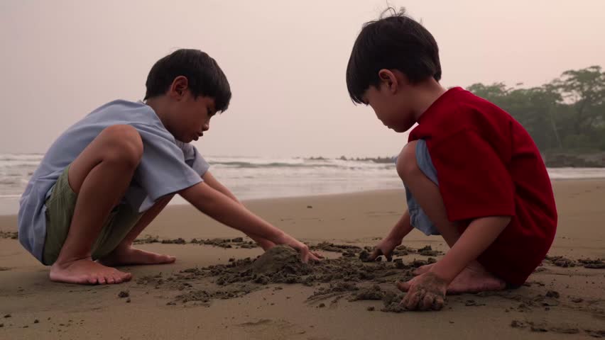 Two children dig in the sand at the beach, building sand castle together