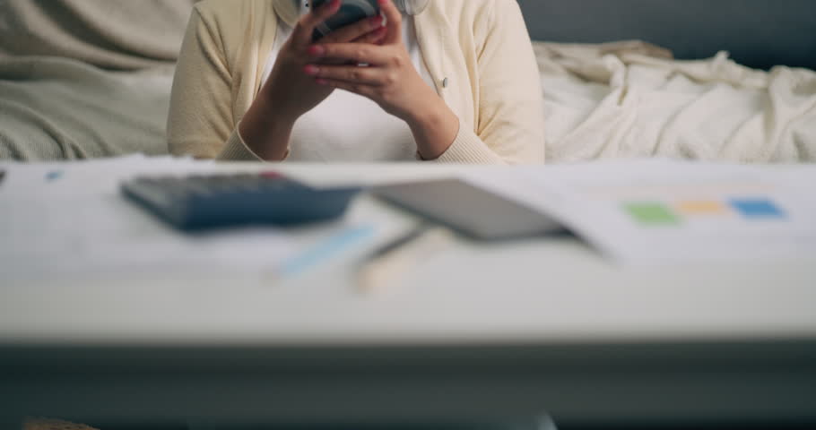Happy Asian female smiling, looking at a mobile phone and checking a successful stock investment portfolio, or playing on social media at home.