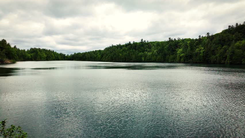 Calm view across Pink Lake (Lac Pink) in Gatineau Park, Quebec, Canada. Quiet freshwater lake surrounded by lush forest under an overcast sky.
