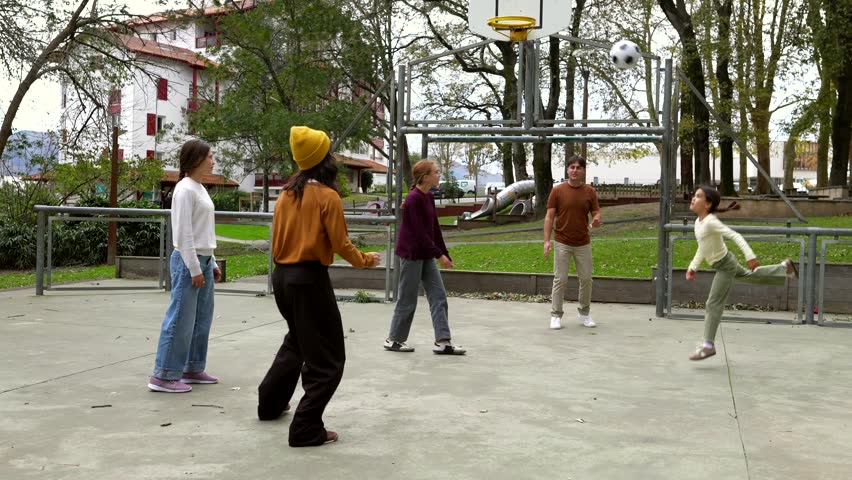 Active family with kids joyfully playing soccer in a public park court, kicking the ball and enjoying quality time together. Cheerful siblings and parents having fun during an outdoor activity