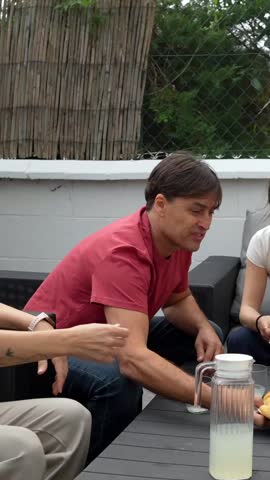 Group of friends and family having a casual outdoor brunch together. People are sitting on a patio. Talking and sharing pastries like croissants and brownies. Creating a relaxed and social atmosphere