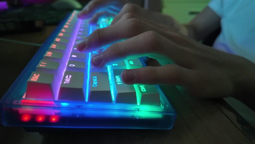 Person typing on a backlit gaming keyboard; typing on a vibrant, colorful gaming keyboard.