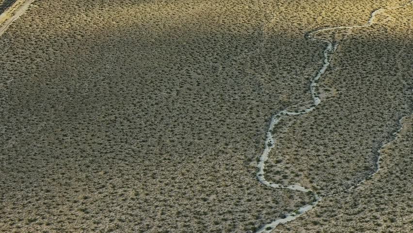 Aerial view shows a dry landscape in the USA with a winding creek cutting through the terrain. The scene captures the natural patterns of the land and water.