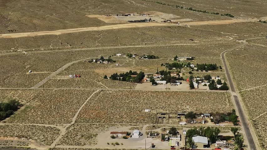 This aerial scene shows a small rural community located in a desert area of the USA. Surrounding land consists of dry terrain and sparse vegetation. Nearby structures are visible.