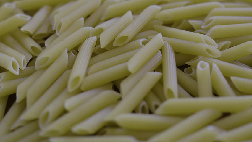 Uncooked Penne Pasta On Wooden Table. Close up of dry italian pasta tubes on rustic wood surface, ideal for cooking, mediterranean cuisine, or food industry themes.