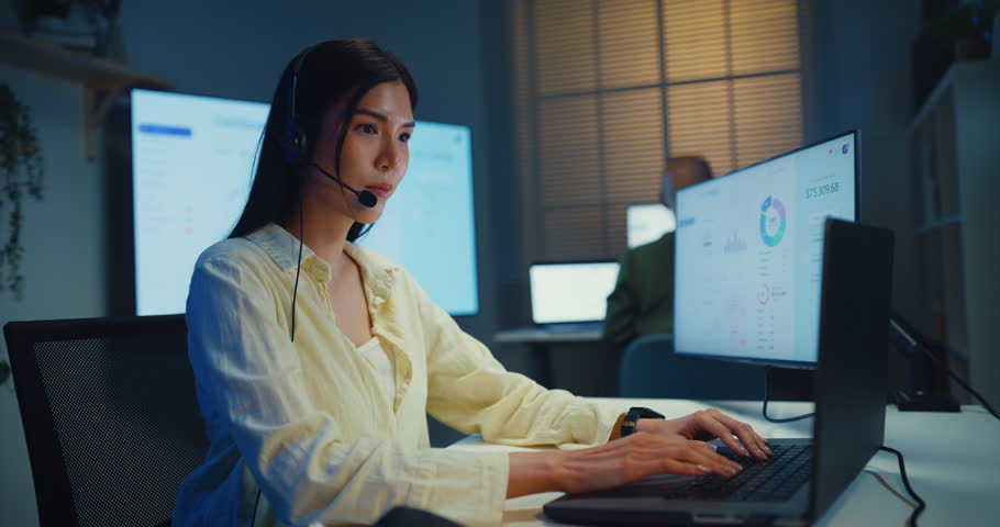 Team young Asian businesswoman working late talk on telephone headset in call center office at night. Corporate customer service support, telemarketing, finance insurance investment advisor concept.