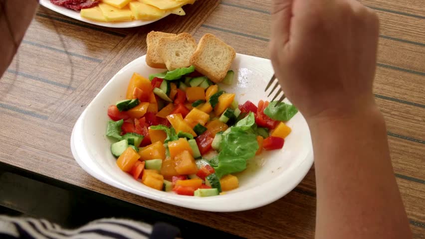 Close up of person eating Salad of mixed colorful chopped vegetables, cucumber, tomato on white plate with wooden table background. Healthy meal prep food concept.