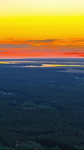 Vivid sunset sky above forest and winding lakes across distant landscape, vertical backdrop of fading glow