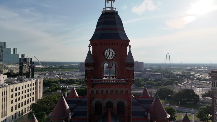 An aerial view shows Dallas County Courthouse with a clock tower, surrounded by Dallas city architecture under a bright sky in Texas