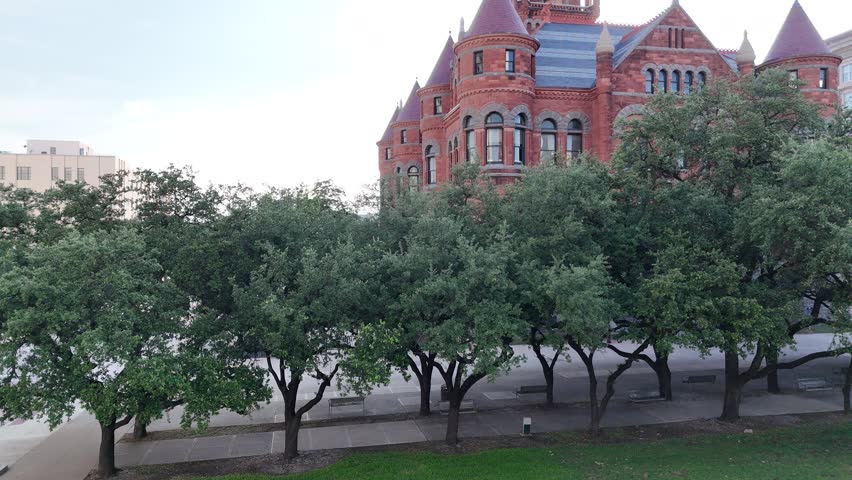 A drone view of Dallas County Courthouse, red brick building with multiple turrets, a clock tower, and ornate architecture, with urban surroundings