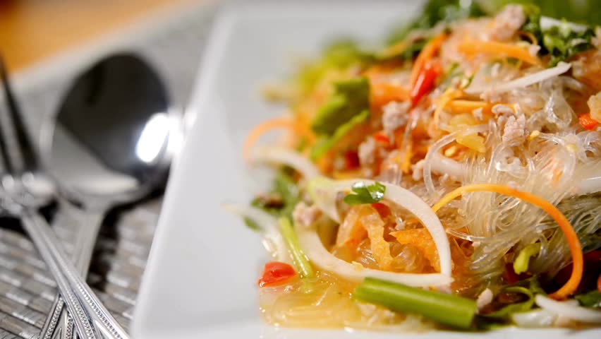 Delicious glass noodle salad featuring fresh vegetables and herbs served elegantly on a white plate. Bright colors enhance the appearance, culinary presentations. vegetarian background healthy