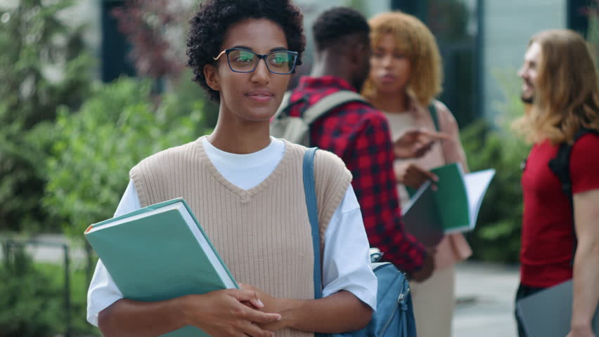 Smiling African American student girl showing thumb up like recommend learning studying in university posing near talking multiethnic students conversation on background in city high school college