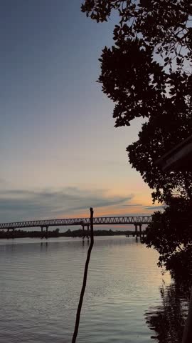 Tranquil sunset over a river bridge, golden hour lighting with silhouette trees, peaceful river landscape