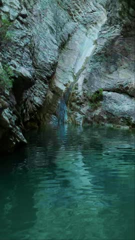 Vertical cinematic shot of a canyon with grey rocky cliffs and a calm blue lake below. Camera is close to the water surface, capturing gentle ripples and a peaceful natural atmosphere.