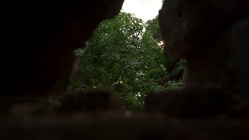 Camera looks through a hole in the stone wall, then tilts down and moves through a doorway at Vat Phou temple in Champasak, Laos.