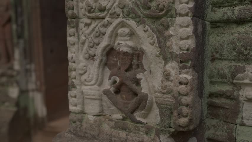 Camera pushes from a carved doorway detail into the Vat Phou temple interior, finishing on the golden Buddha statue framed by ancient stone columns.